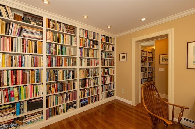 living area featuring bookshelves, wood finished floors, baseboard heating, and ornamental molding