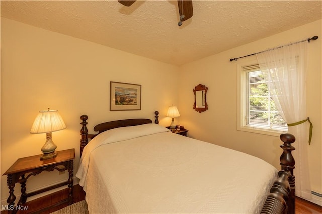 bedroom featuring baseboard heating, a textured ceiling, a ceiling fan, and wood finished floors