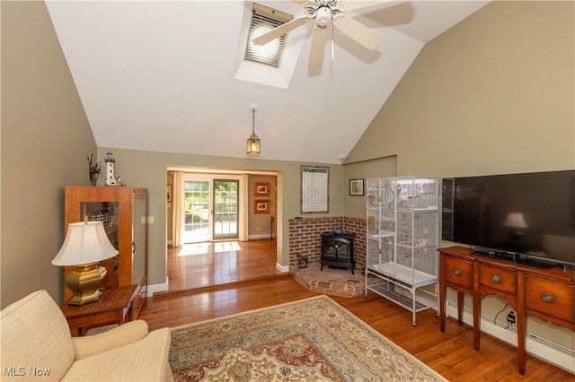 living area featuring baseboards, ceiling fan, a skylight, a wood stove, and wood finished floors