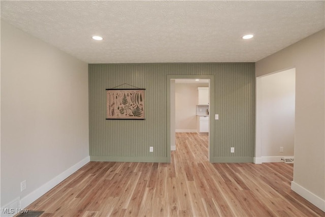 spare room featuring a textured ceiling, light wood-style floors, and baseboards