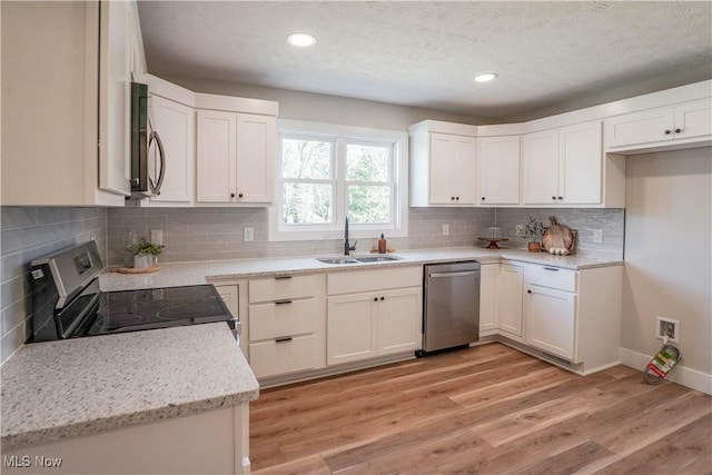 kitchen with a sink, white cabinets, light wood-style floors, appliances with stainless steel finishes, and tasteful backsplash