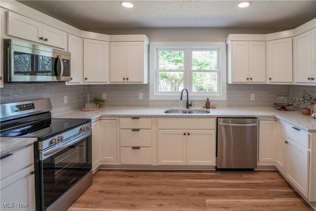 kitchen with white cabinetry, stainless steel appliances, light wood-type flooring, and a sink