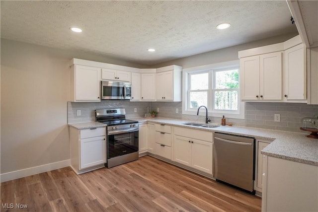 kitchen with light wood finished floors, stainless steel appliances, baseboards, and a sink