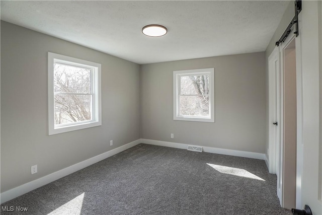 unfurnished bedroom with a barn door, baseboards, carpet floors, and a textured ceiling