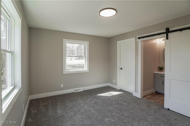 unfurnished bedroom with visible vents, baseboards, carpet, and a barn door