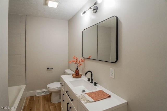 bathroom with visible vents, toilet, a bathing tub, wood finished floors, and vanity