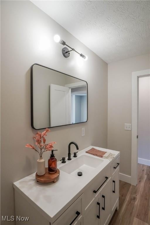 bathroom with vanity, wood finished floors, baseboards, and a textured ceiling