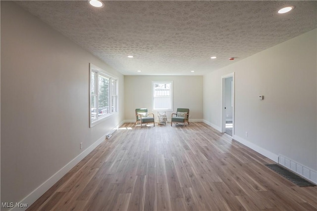 unfurnished room featuring wood finished floors, visible vents, baseboards, recessed lighting, and a textured ceiling