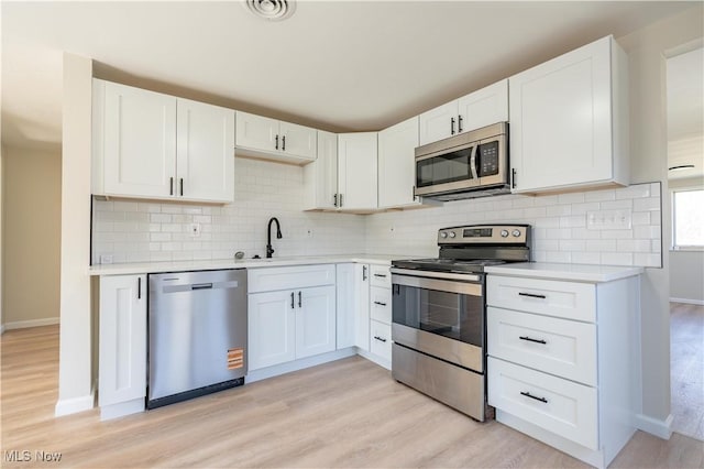 kitchen with light countertops, appliances with stainless steel finishes, light wood-style floors, white cabinetry, and a sink