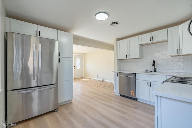 kitchen with tasteful backsplash, light countertops, appliances with stainless steel finishes, light wood-style floors, and a sink