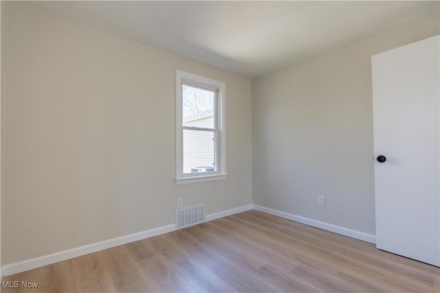 empty room with visible vents, light wood-type flooring, and baseboards