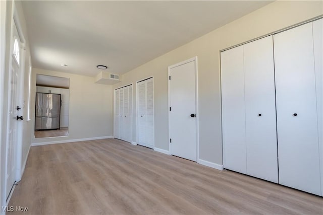 unfurnished bedroom featuring light wood finished floors, stainless steel refrigerator, visible vents, and multiple closets