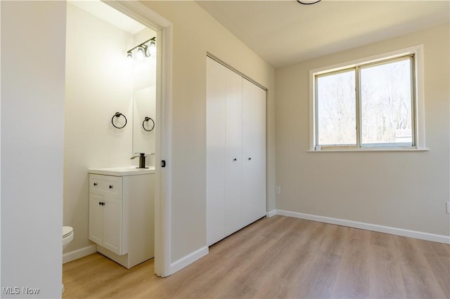 unfurnished bedroom with a closet, light wood-type flooring, baseboards, and a sink