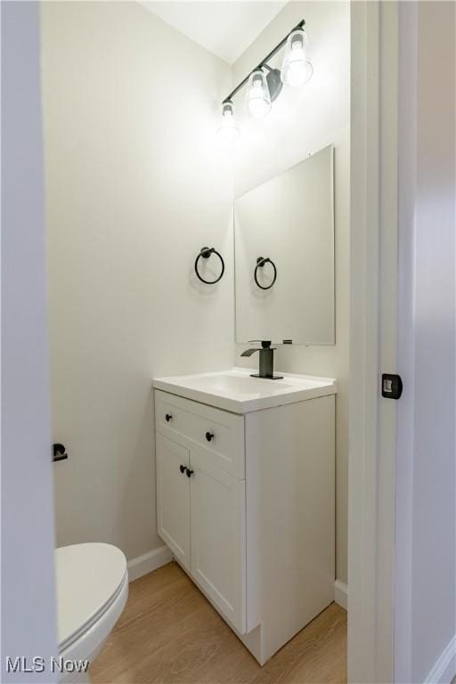 bathroom with baseboards, toilet, wood finished floors, and vanity