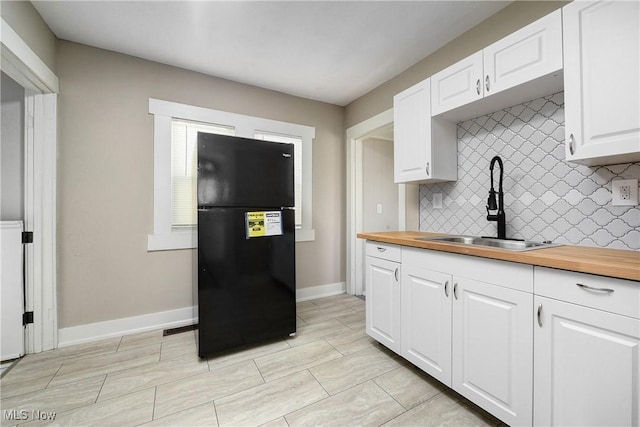 kitchen featuring freestanding refrigerator, a sink, wood counters, white cabinetry, and backsplash