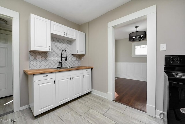 kitchen featuring black range with electric stovetop, a sink, wood counters, tasteful backsplash, and white cabinets