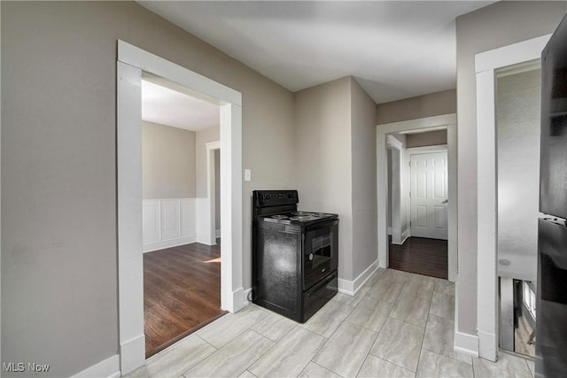 kitchen with a decorative wall, wainscoting, black range with electric cooktop, and light wood-style floors