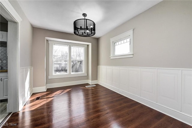 unfurnished dining area with visible vents, dark wood-type flooring, a notable chandelier, and baseboards