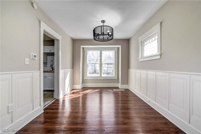 unfurnished dining area featuring visible vents, plenty of natural light, an inviting chandelier, and dark wood-style flooring