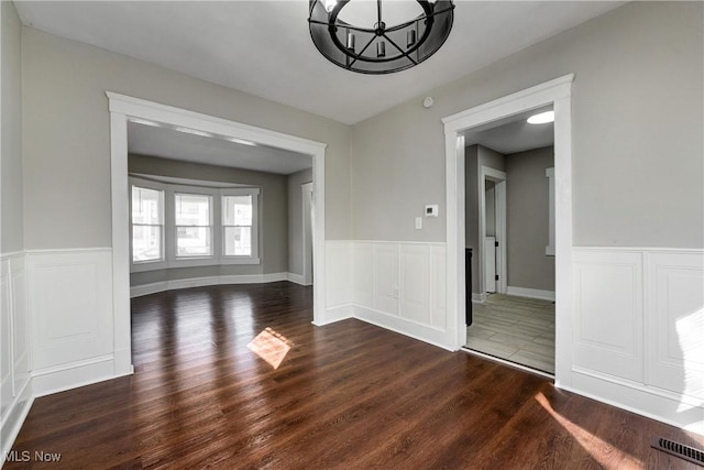 empty room with a chandelier, visible vents, wainscoting, and wood finished floors