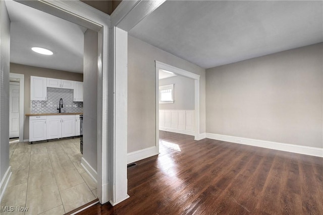 interior space featuring a wainscoted wall, baseboards, light wood-style floors, and a sink