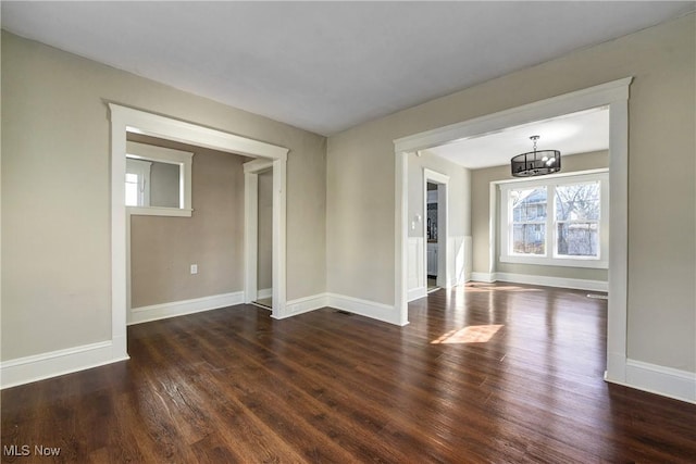 empty room with dark wood-type flooring, baseboards, and a chandelier