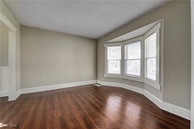 spare room with baseboards and dark wood-type flooring