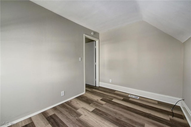 spare room featuring dark wood-style floors, visible vents, baseboards, and vaulted ceiling