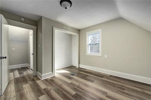 unfurnished bedroom with dark wood-style floors, visible vents, baseboards, lofted ceiling, and a closet