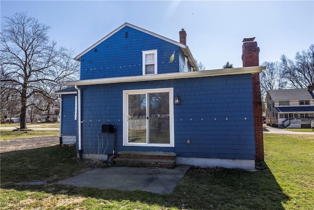 back of house featuring entry steps, a lawn, and a chimney