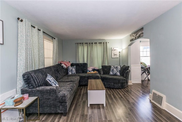 living area featuring visible vents, arched walkways, baseboards, and wood finished floors