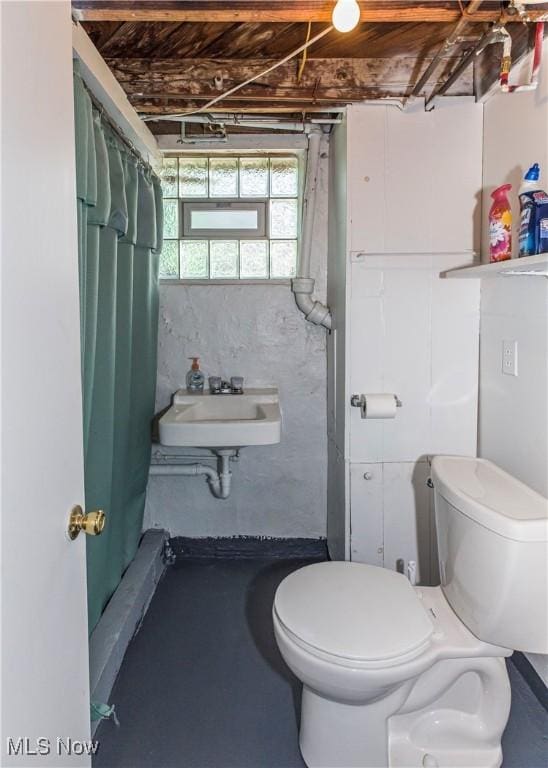 bathroom with curtained shower, toilet, concrete floors, and a sink