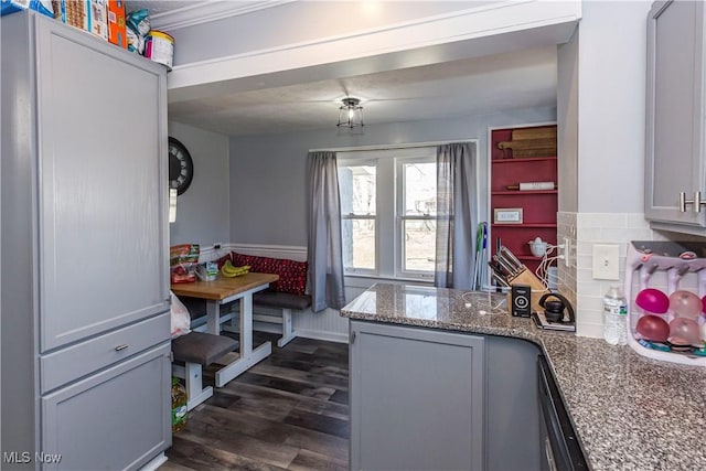 kitchen with a wainscoted wall, dark wood-type flooring, stone countertops, black dishwasher, and a peninsula