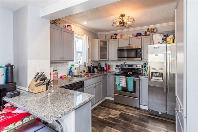 kitchen with a peninsula, gray cabinets, a sink, dark wood-type flooring, and appliances with stainless steel finishes