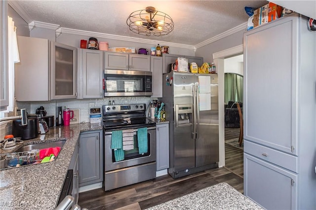 kitchen featuring dark wood finished floors, gray cabinetry, stainless steel appliances, crown molding, and backsplash