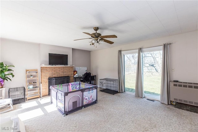 carpeted living room with visible vents, radiator, a fireplace, and a ceiling fan