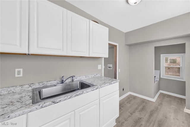 kitchen with light stone counters, baseboards, light wood-style flooring, a sink, and white cabinets