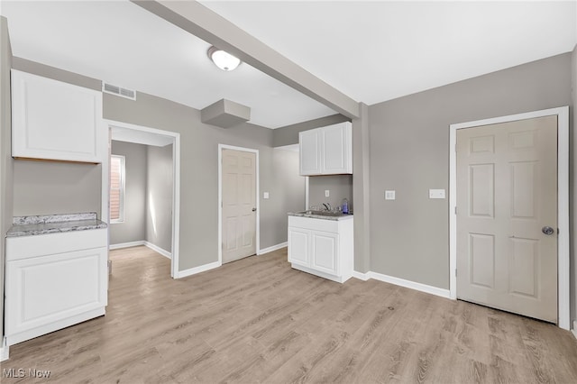 unfurnished living room featuring a sink, visible vents, baseboards, and light wood-style floors