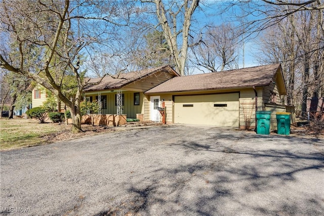 view of front of home featuring aphalt driveway, covered porch, roof with shingles, and an attached garage