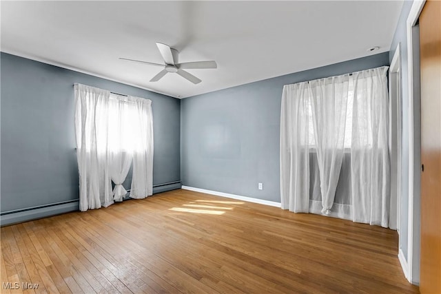 empty room featuring hardwood / wood-style flooring, a ceiling fan, baseboards, and baseboard heating