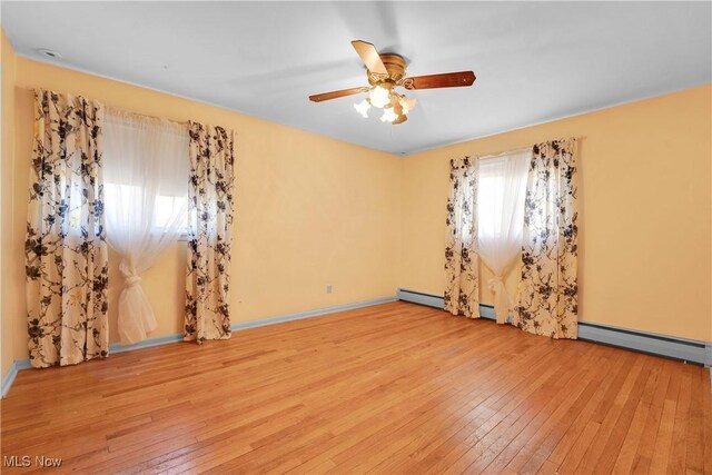 unfurnished room with a baseboard heating unit, baseboards, hardwood / wood-style floors, baseboard heating, and a ceiling fan