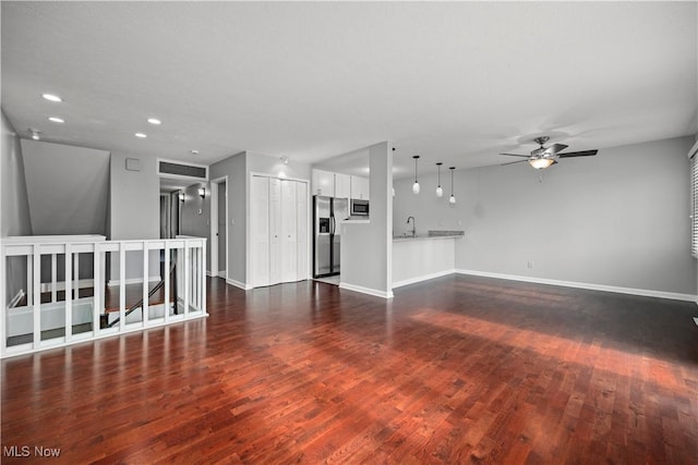 unfurnished living room featuring dark wood finished floors, baseboards, a ceiling fan, and a sink