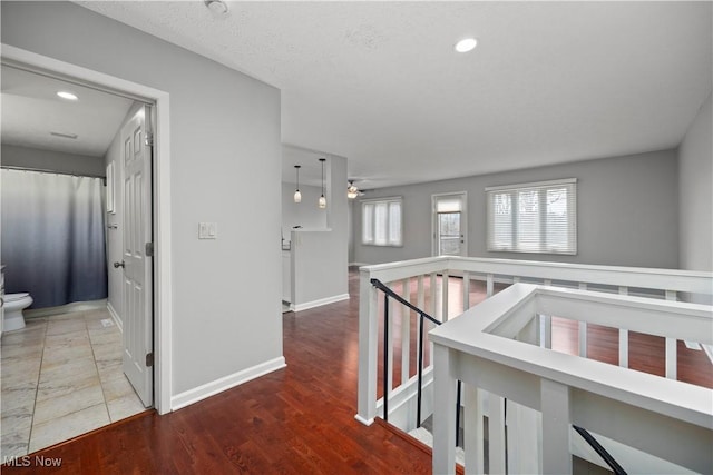 corridor with baseboards, an upstairs landing, a healthy amount of sunlight, and wood finished floors