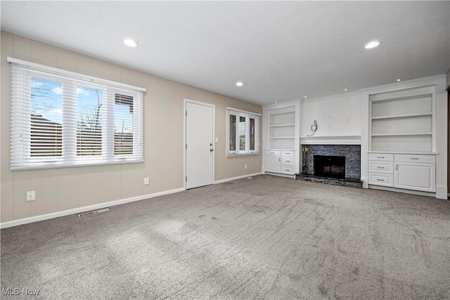 unfurnished living room featuring built in shelves, a fireplace with raised hearth, recessed lighting, carpet flooring, and baseboards