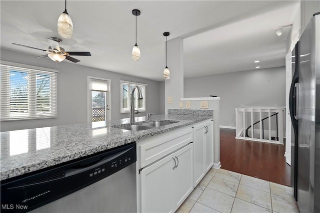 kitchen featuring light stone counters, stainless steel dishwasher, freestanding refrigerator, white cabinets, and a sink