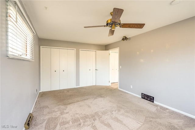 unfurnished bedroom featuring ceiling fan, two closets, baseboards, and carpet floors