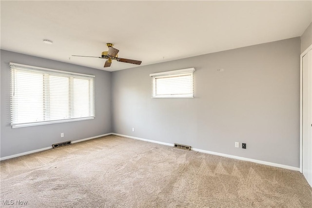 carpeted spare room with visible vents, baseboards, and ceiling fan