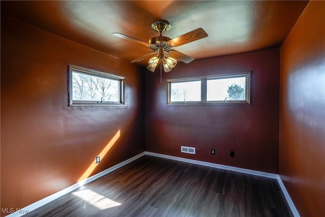 empty room with dark wood-style floors, visible vents, baseboards, and ceiling fan