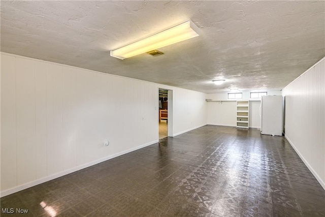 below grade area with baseboards, visible vents, freestanding refrigerator, a textured ceiling, and tile patterned floors