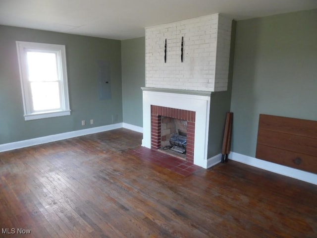 unfurnished living room with dark wood finished floors, a brick fireplace, electric panel, and baseboards